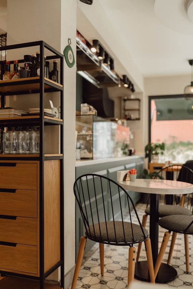 A cozy corner of a modern cafe with stylish furniture and shelving stocked with various items.