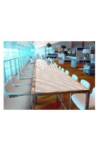 A Barcelona Long Bar Table with white chairs in front of it.