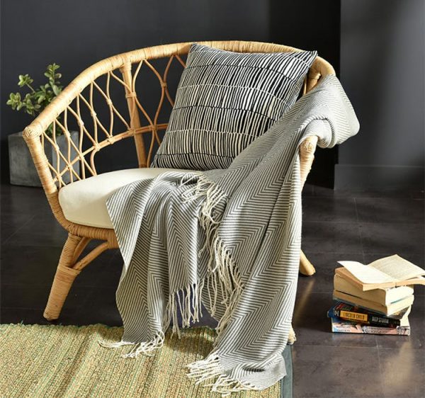 a wicker chair with a throw in grey striped pattern and books on it
