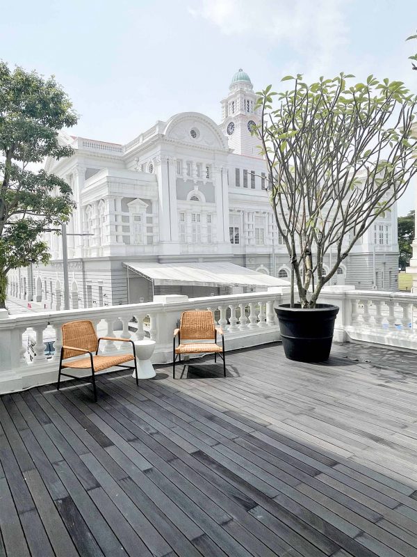 a wooden deck with cayman rattan armchairs and a tree in front of a building