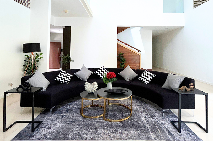 A modern living room with a curved black sofa, black and white chevron pillows, nested round coffee tables, a grey rug, and decorative plants.